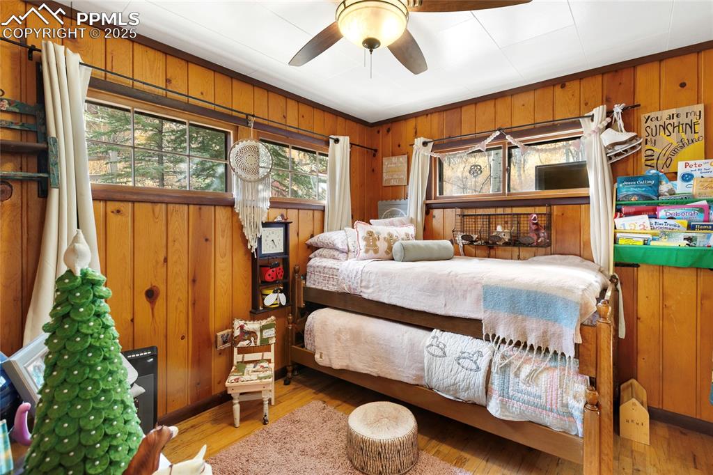 Bedroom with wood walls, wood finished floors, and ceiling fan