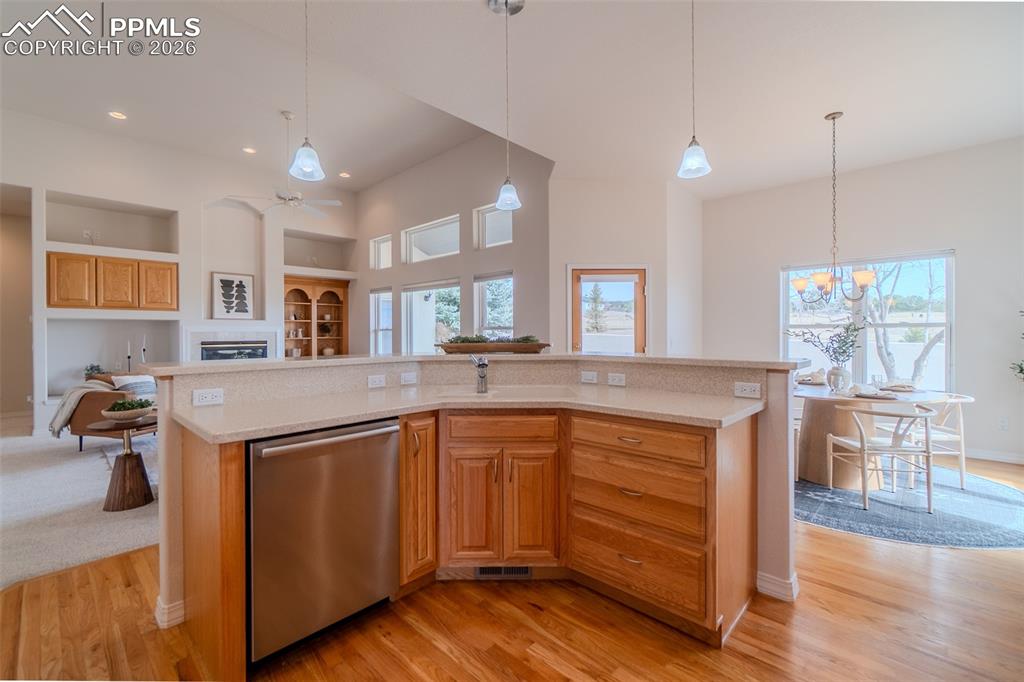 Kitchen with stainless steel dishwasher, open floor plan, a high ceiling, light wood finished floors, and built in shelves