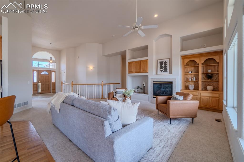 Living area featuring built in features, a ceiling fan, light colored carpet, a glass covered fireplace, and a high ceiling