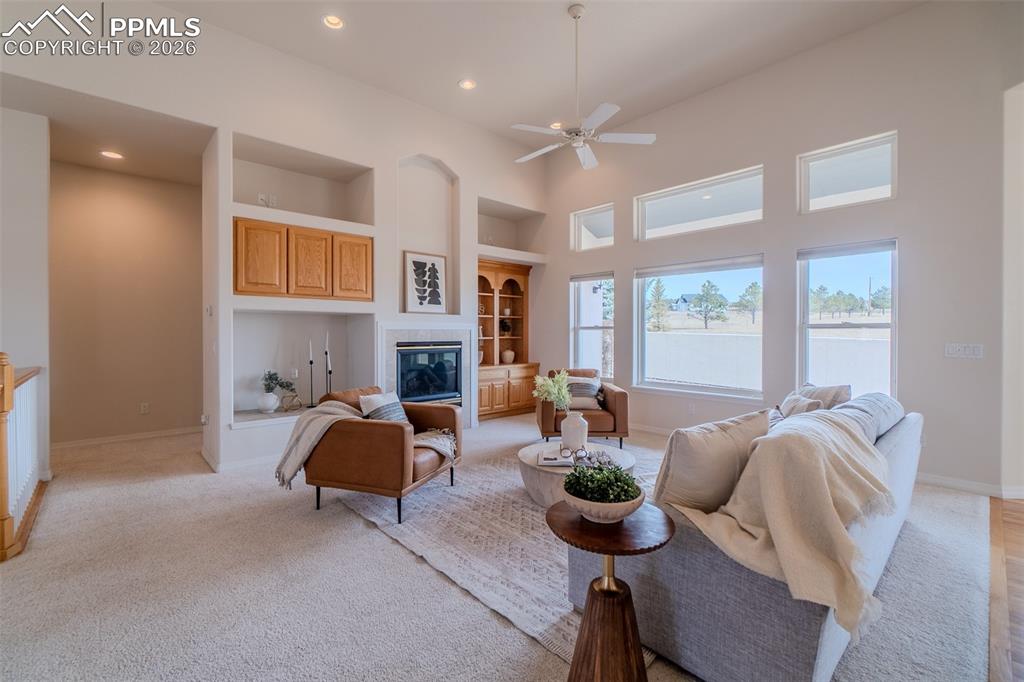 Living room with a high ceiling, built in features, a ceiling fan, a glass covered fireplace, and recessed lighting