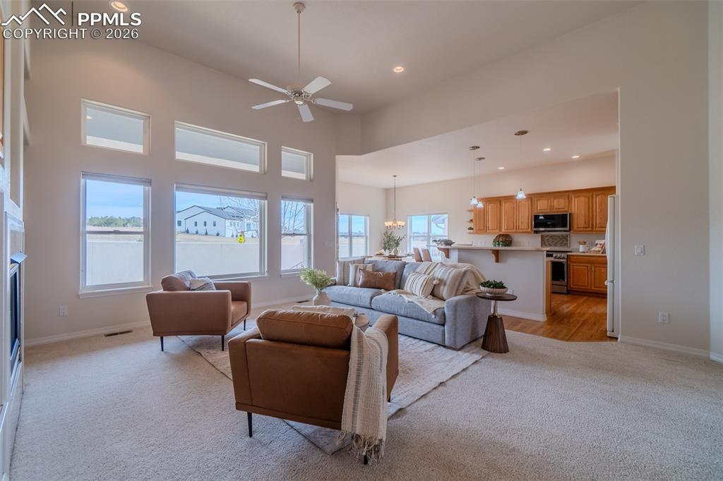 Living room with a ceiling fan, light carpet, a high ceiling, a fireplace, and hanging lights