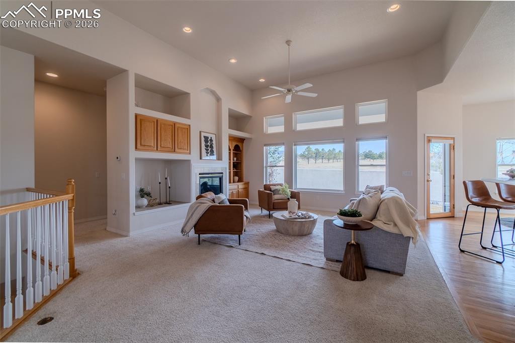 Living room with a high ceiling, built in features, a ceiling fan, a glass covered fireplace, and recessed lighting