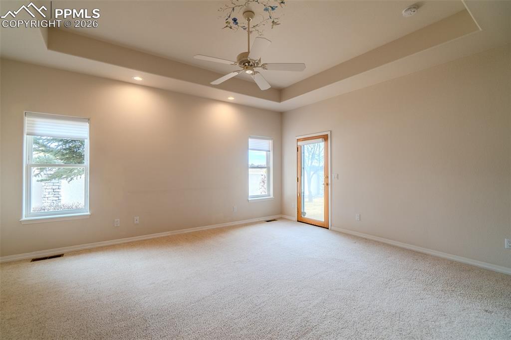 Primary featuring a ceiling fan, a tray ceiling, light colored carpet, and recessed lighting
