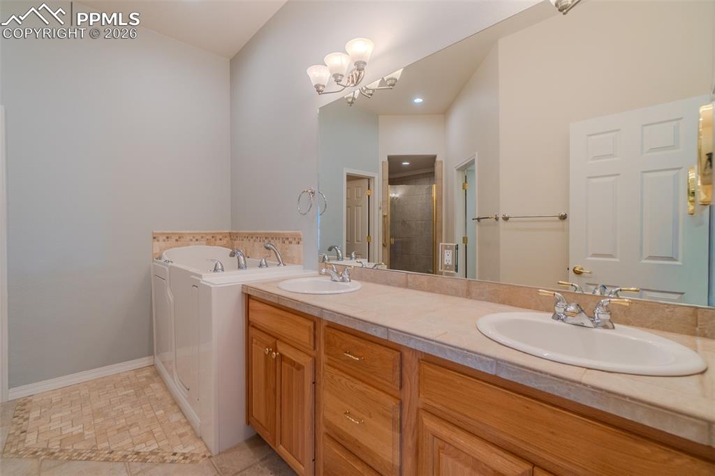Five piece bathroom with double vanity, suspended lighting, a walk in bath, shower, and walk in closet 