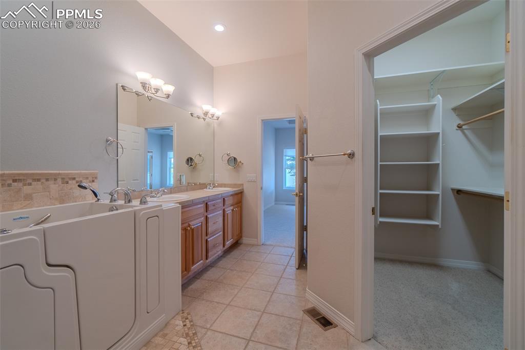 Bathroom with double vanity, light tile patterned flooring, a spacious closet, a garden tub and walk in closet
