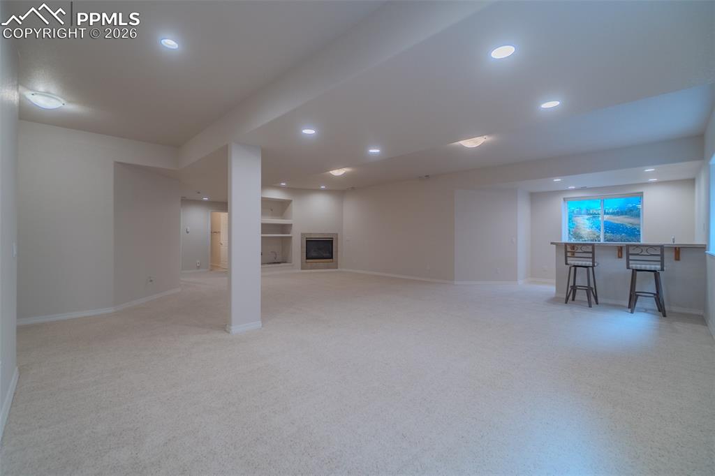 Finished below grade area with light colored carpet, recessed lighting, a fireplace, and bar area