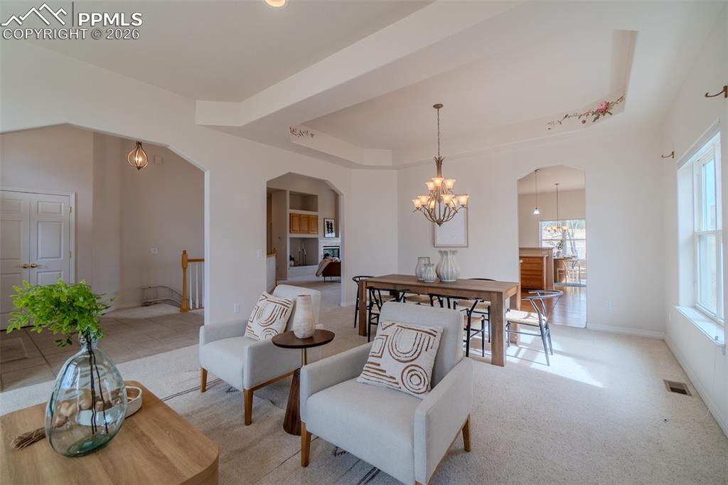 Living area with a raised ceiling, arched walkways, carpet floors, and a chandelier