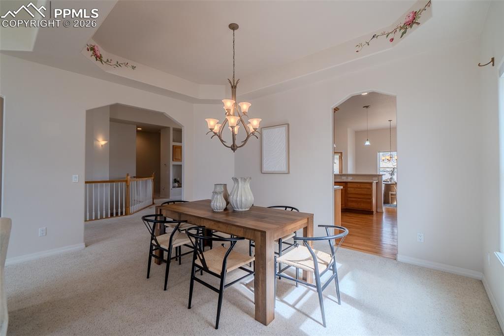Dining space featuring a tray ceiling, arched walkways, light colored carpet, and suspended lighting