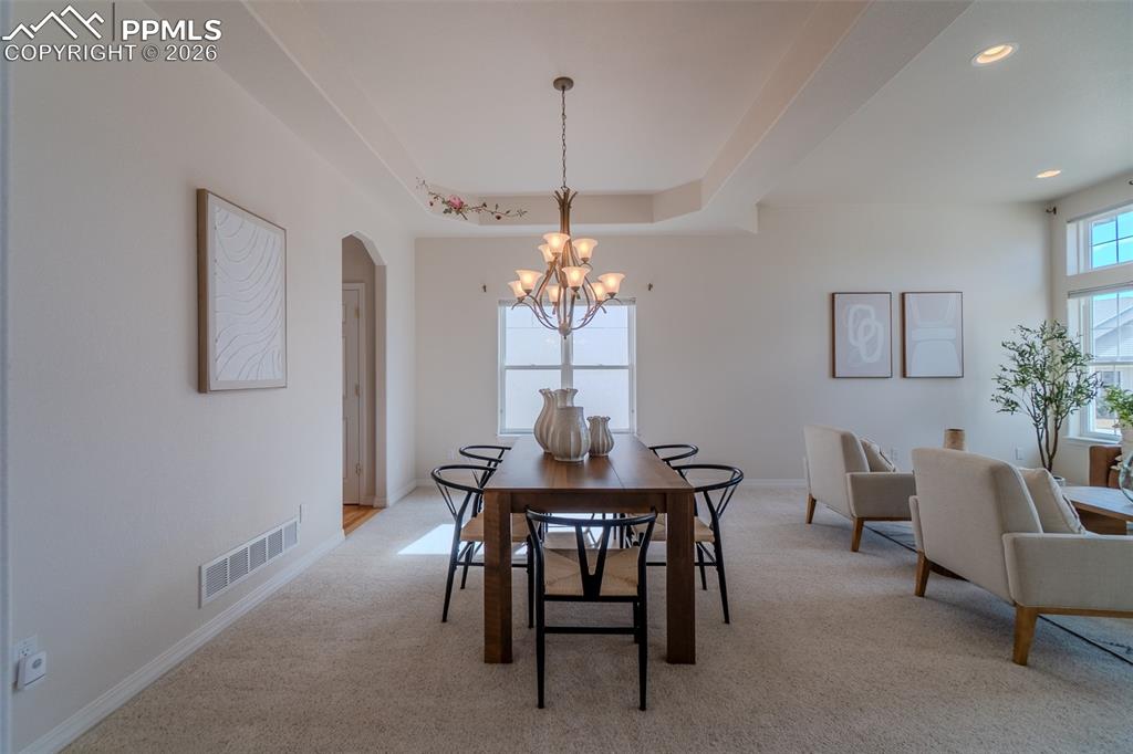 Dining room with arched walkways, light colored carpet, suspended lighting, and a tray ceiling