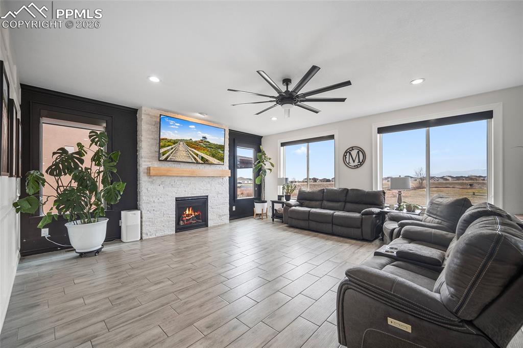 Living room featuring recessed lighting, a stone fireplace, a ceiling fan, and wood finished floors