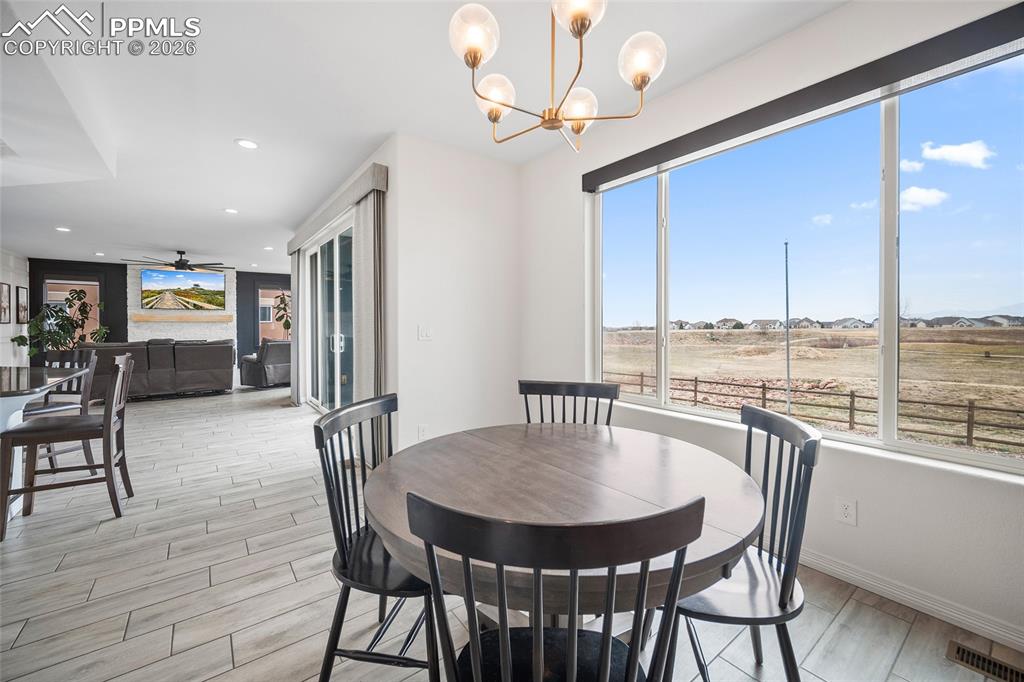 Dining area featuring light wood-type flooring, baseboards, recessed lighting, visible vents, and ceiling fan with notable chandelier