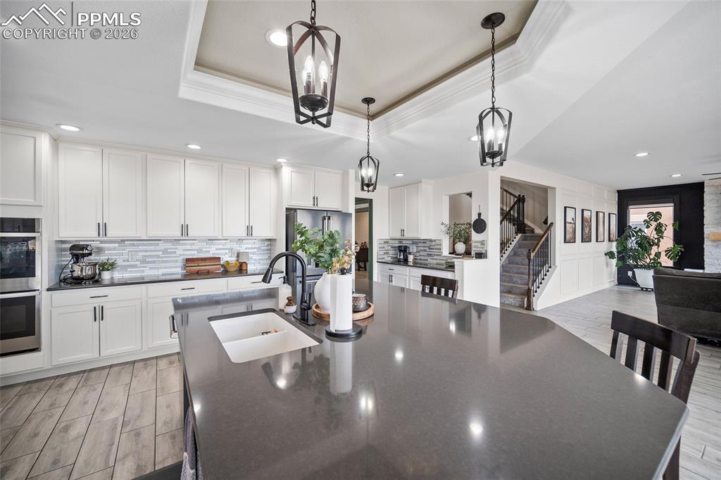 Kitchen with a sink, a kitchen island with sink, a tray ceiling, stainless steel appliances, and backsplash