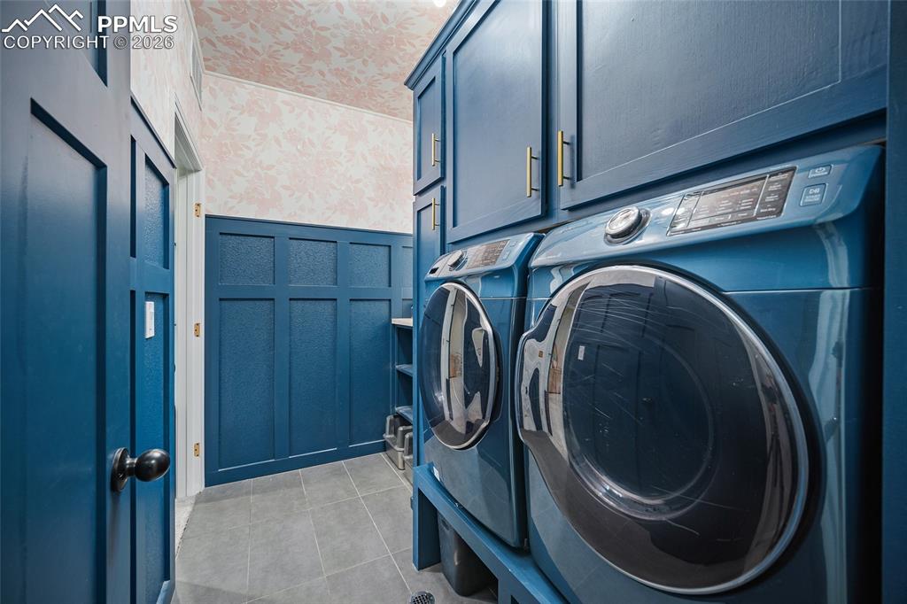 Washroom featuring a decorative wall, independent washer and dryer, light tile patterned flooring, wainscoting, and cabinet space