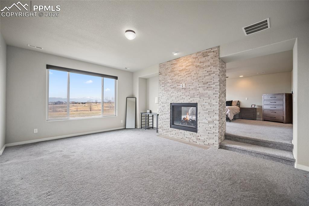 Unfurnished living room with carpet flooring, visible vents, baseboards, and a brick fireplace