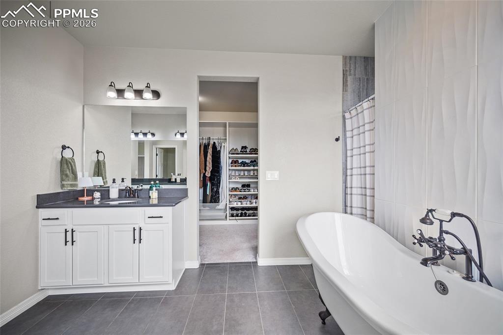 Full bathroom featuring a freestanding bath, a spacious closet, vanity, tile patterned floors, and tiled shower