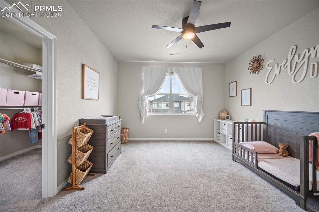 Carpeted bedroom with baseboards, a ceiling fan, and a crib