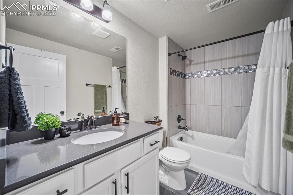 Full bath featuring shower / bath combination with curtain, vanity, visible vents, toilet, and tile patterned floors