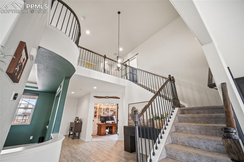 Stairs featuring recessed lighting, wood finished floors, and a towering ceiling