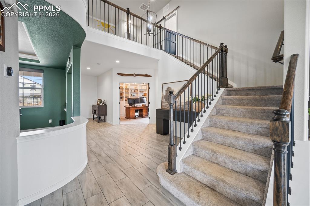 Stairs featuring recessed lighting, open railing, wood finished floors, and a towering ceiling