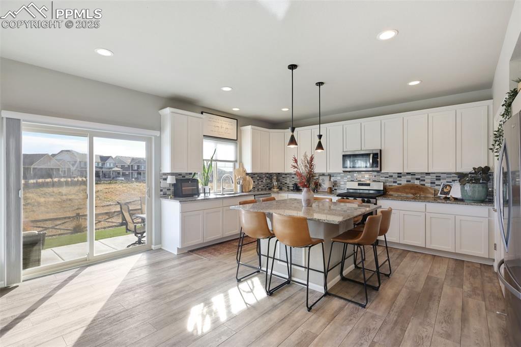 Kitchen with a breakfast bar, hanging light fixtures, light stone counters, white cabinetry, and a center island