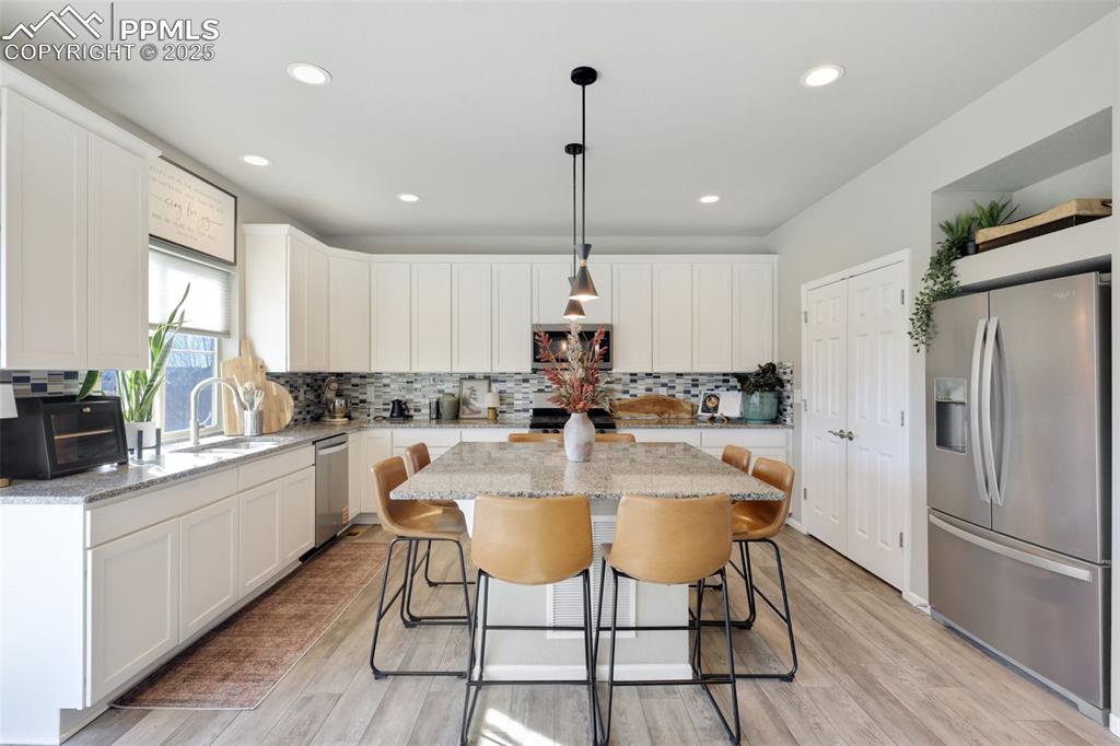 Kitchen with appliances with stainless steel finishes, white cabinetry, a kitchen bar, and recessed lighting