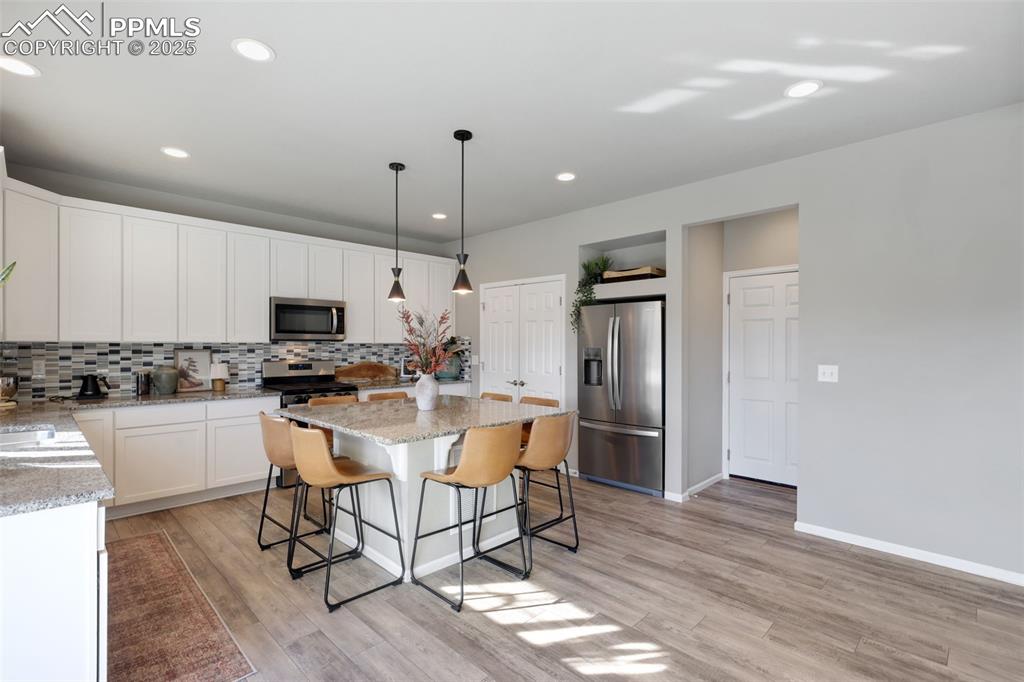 Kitchen featuring hanging light fixtures, a kitchen breakfast bar, stainless steel appliances, white cabinets, and light stone countertops