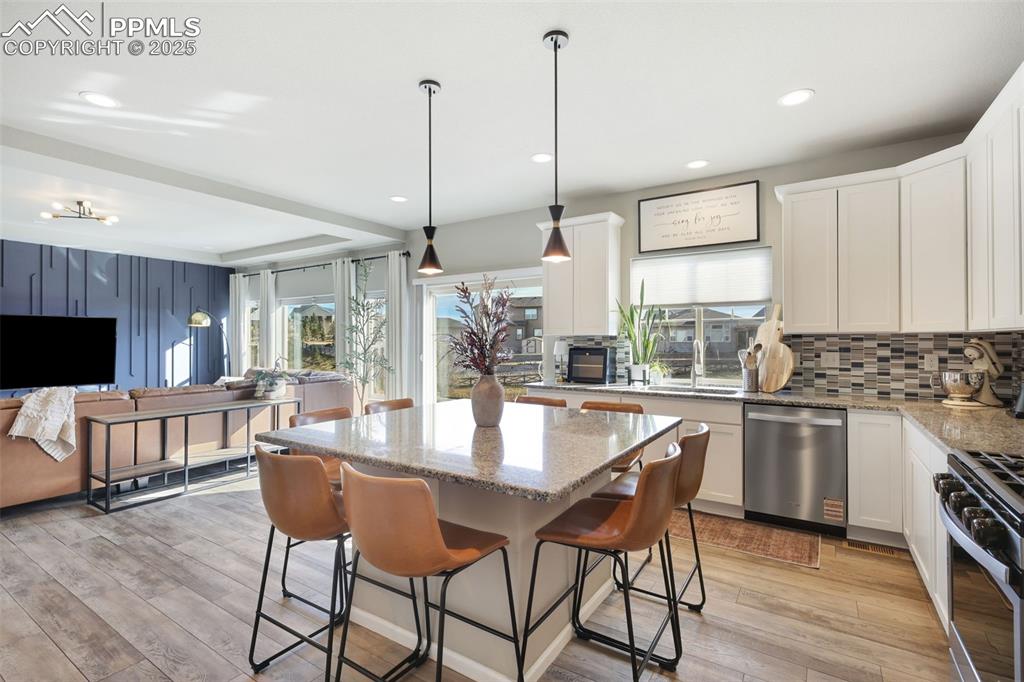 Kitchen with light stone counters, decorative light fixtures, range with gas cooktop, white cabinetry, and recessed lighting