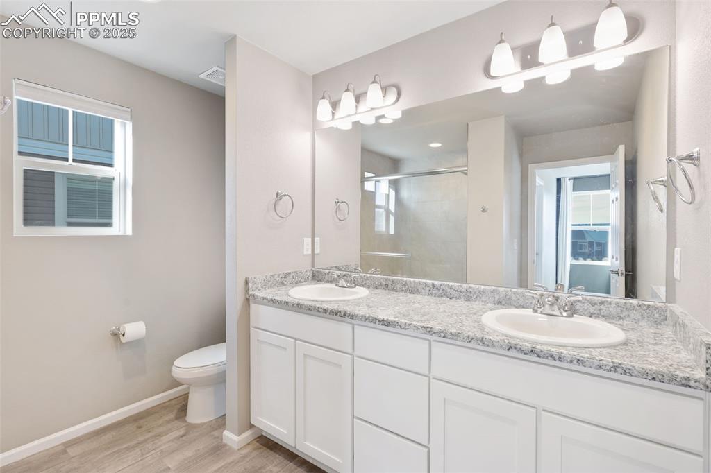 Bathroom with double vanity, a stall shower, and light wood-style flooring