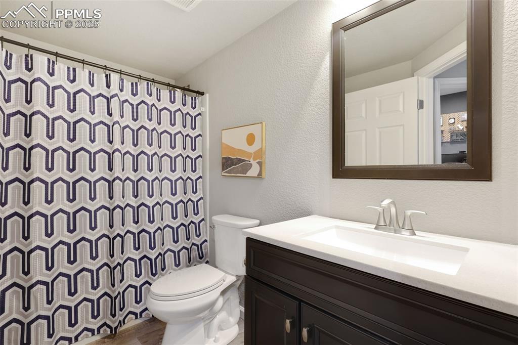Bathroom with a textured wall, vanity, a shower with curtain, and wood finished floors