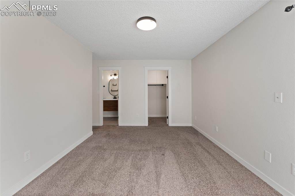 Unfurnished bedroom featuring a spacious closet, carpet, ensuite bathroom, and a textured ceiling