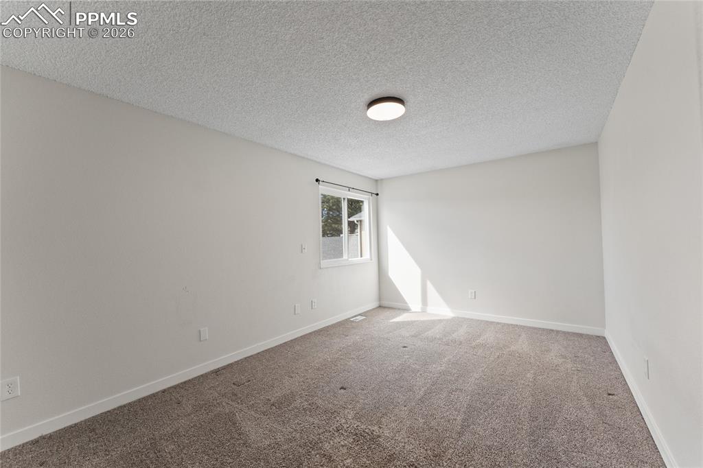 Carpeted empty room with a textured ceiling and baseboards