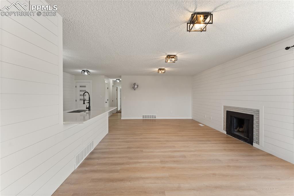 Unfurnished living room with light wood-type flooring, a fireplace, a textured ceiling, and wooden walls