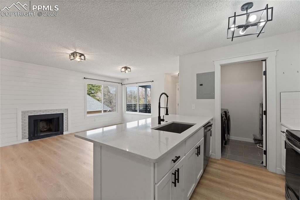 Kitchen with a fireplace, a peninsula, light wood-style flooring, a textured ceiling, and light stone countertops
