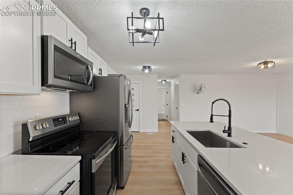 Kitchen with stainless steel appliances, white cabinets, light wood-style floors, and a textured ceiling