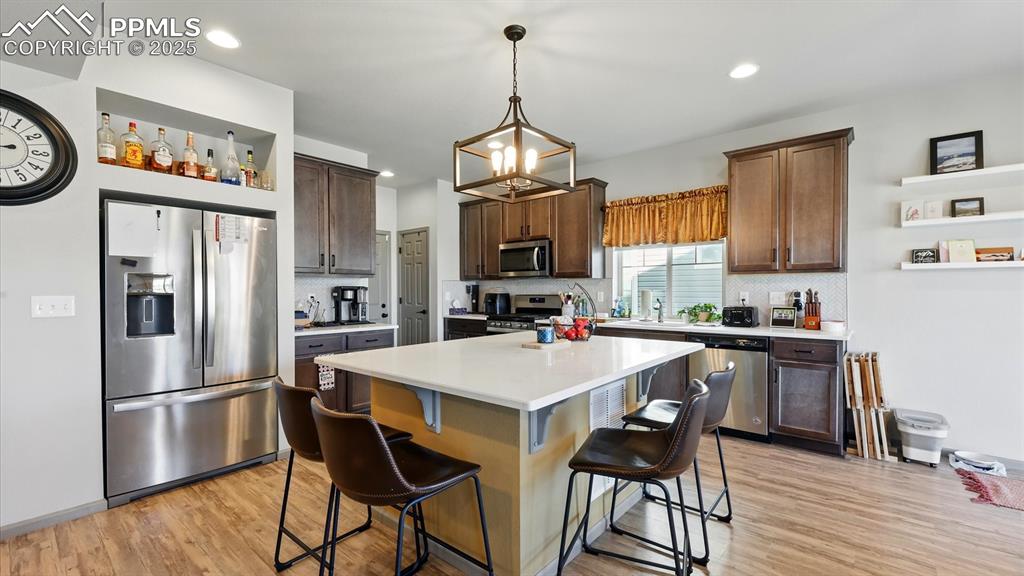 The Island Kitchen boasts a modern light fixture, breakfast bar, pantry, dark cabinets with solid countertops, and stainless steel appliances.