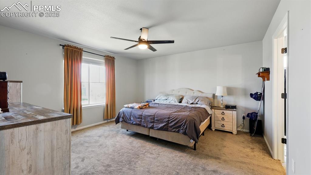 Upper Level Primary Bedroom with neutral carpet, a lighted ceiling fan, walk in closet, and adjoining shower bathroom.