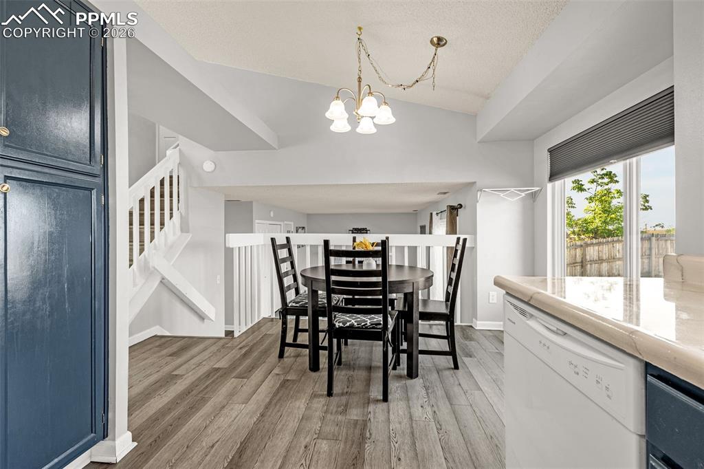 Dining space featuring vaulted ceiling, light wood finished floors, a chandelier, stairway, and a textured ceiling