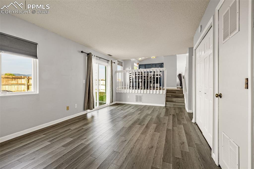 Spare room with a textured ceiling, plenty of natural light, stairs, and dark wood finished floors