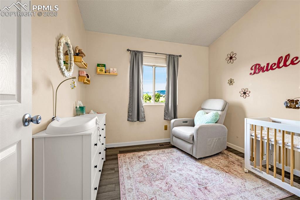 Bedroom with a crib, wood finished floors, a textured ceiling, and lofted ceiling