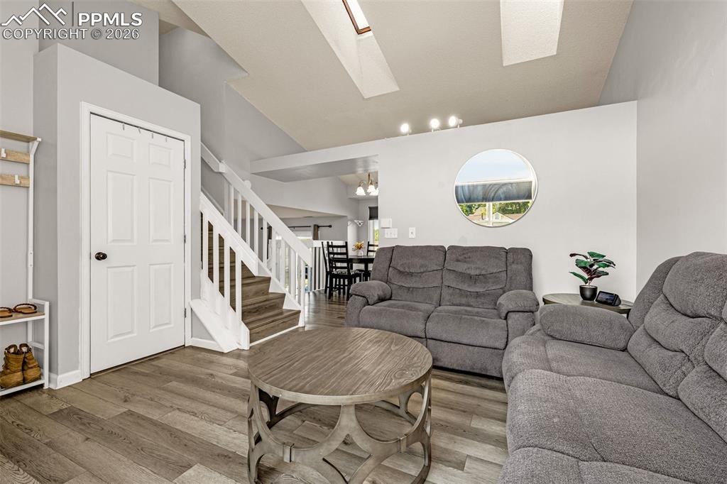 Living room featuring vaulted ceiling, light wood-style floors, stairway, and a skylight