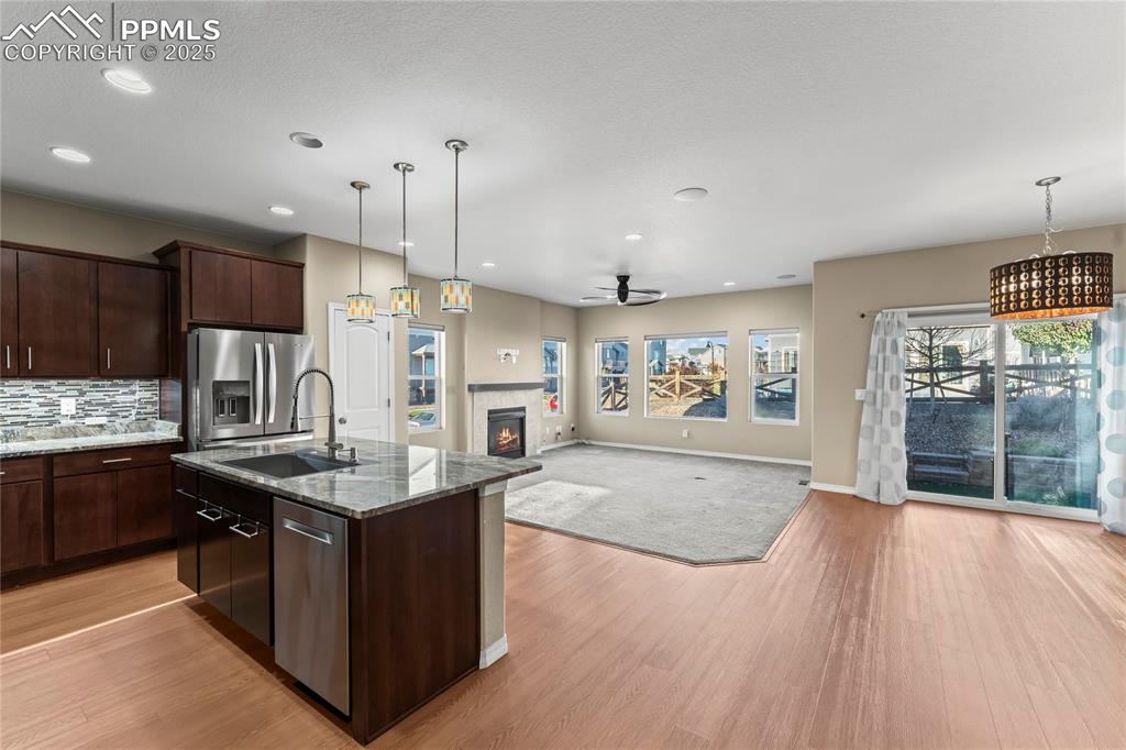 Kitchen with pendant lighting, open floor plan, dark stone countertops, an island with sink, and dark brown cabinetry