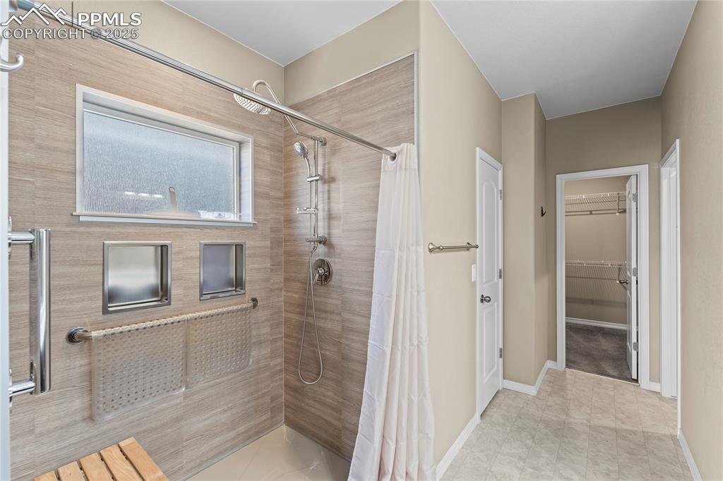 Bathroom with a tile shower, a walk in closet, and light tile patterned floors