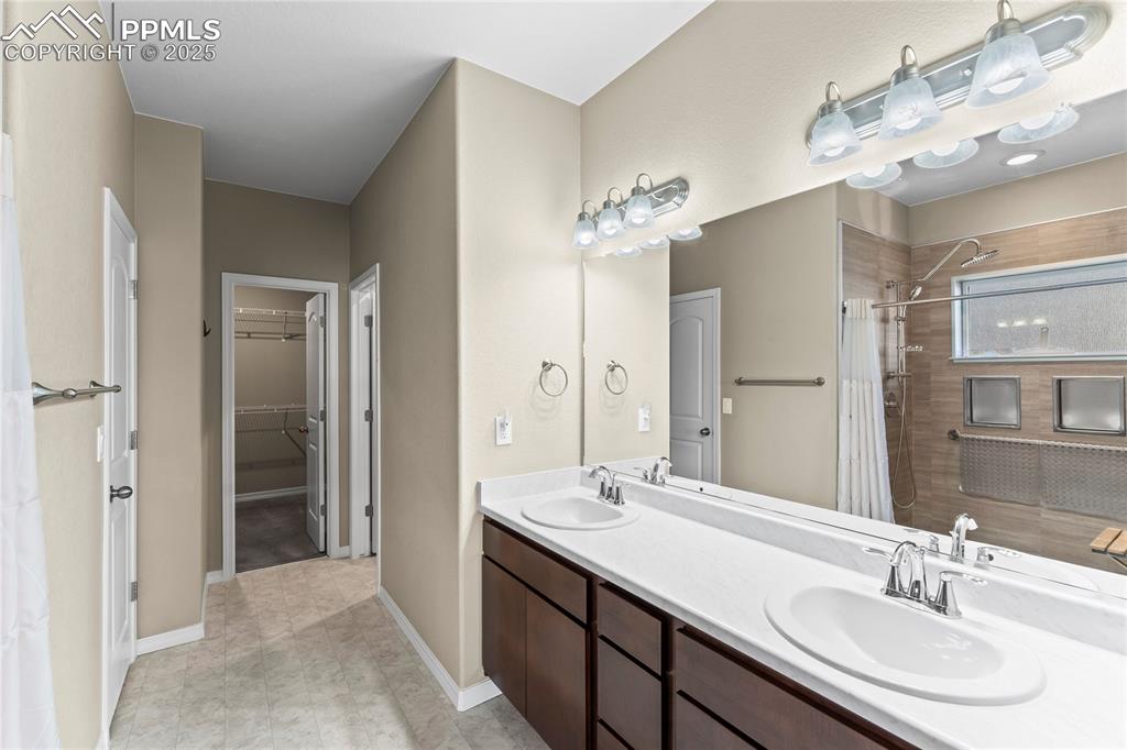 Bathroom with double vanity, a walk in closet, and a tile shower