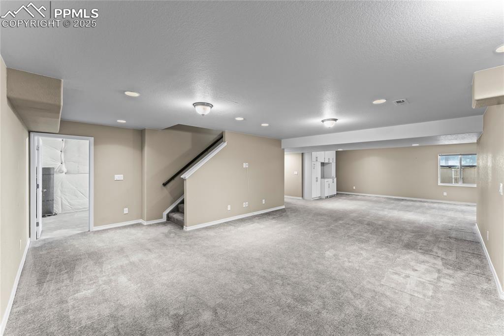Basement with light colored carpet, stairs, and a textured ceiling