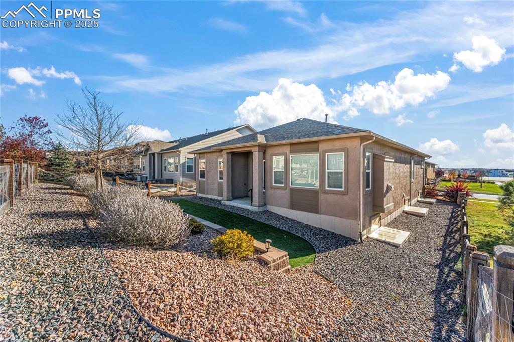 View of front facade featuring a fenced backyard, roof with shingles, stucco siding, and a patio area
