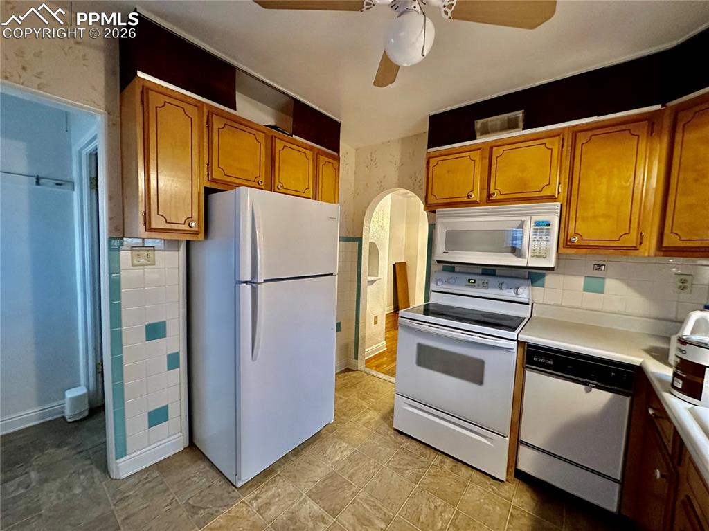 Kitchen featuring white appliances, arched walkways, light countertops, brown cabinets, and ceiling fan