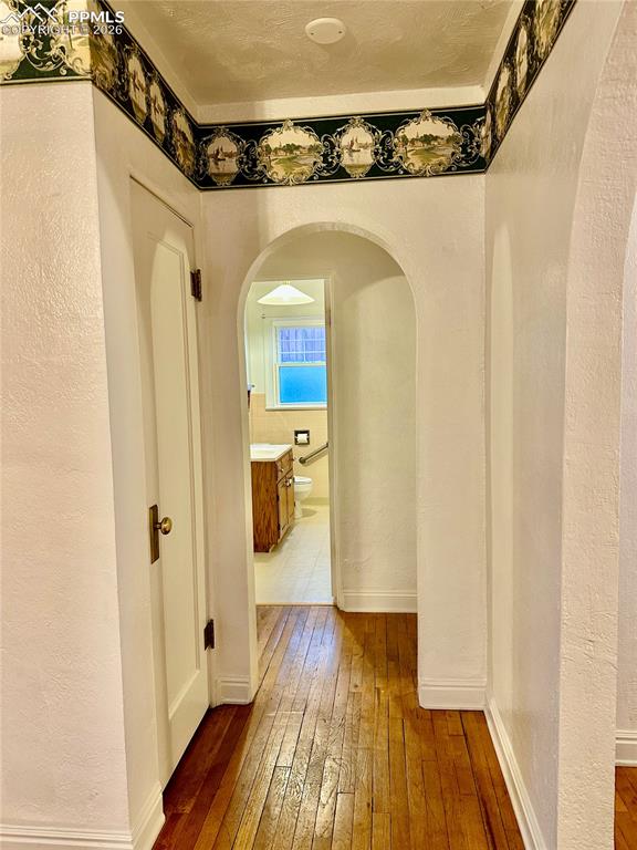 Hallway with a textured wall, dark wood-style floors, and arched walkways
