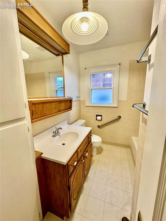 Bathroom featuring vanity, light tile patterned flooring, wainscoting, tile walls, and washtub / shower combination