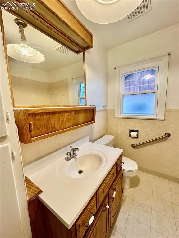 Bathroom with vanity, wainscoting, plenty of natural light, light tile patterned floors, and tile walls