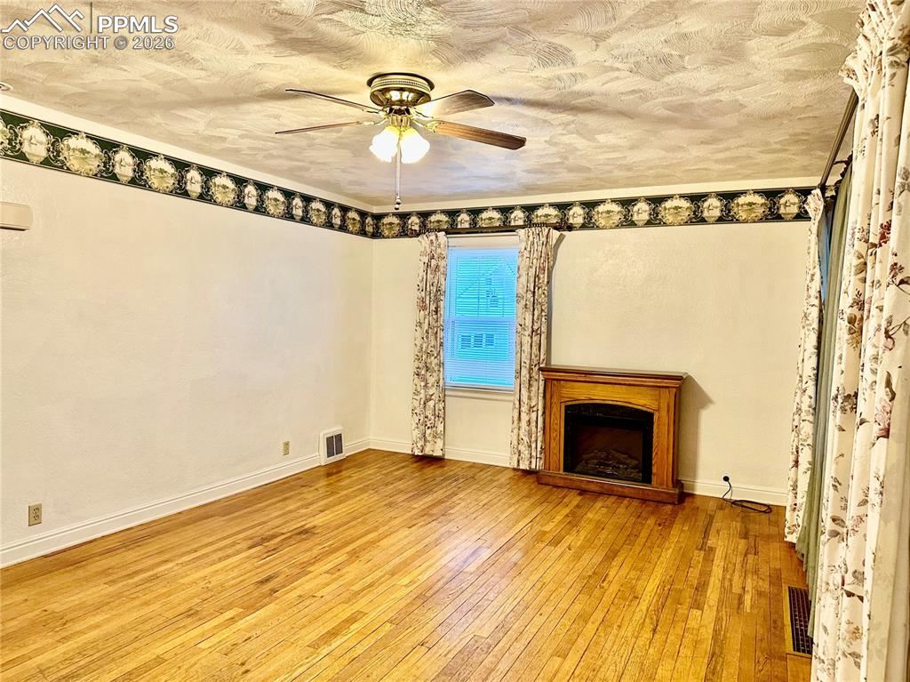 Unfurnished living room featuring a fireplace, light wood-type flooring, a textured ceiling, and a ceiling fan